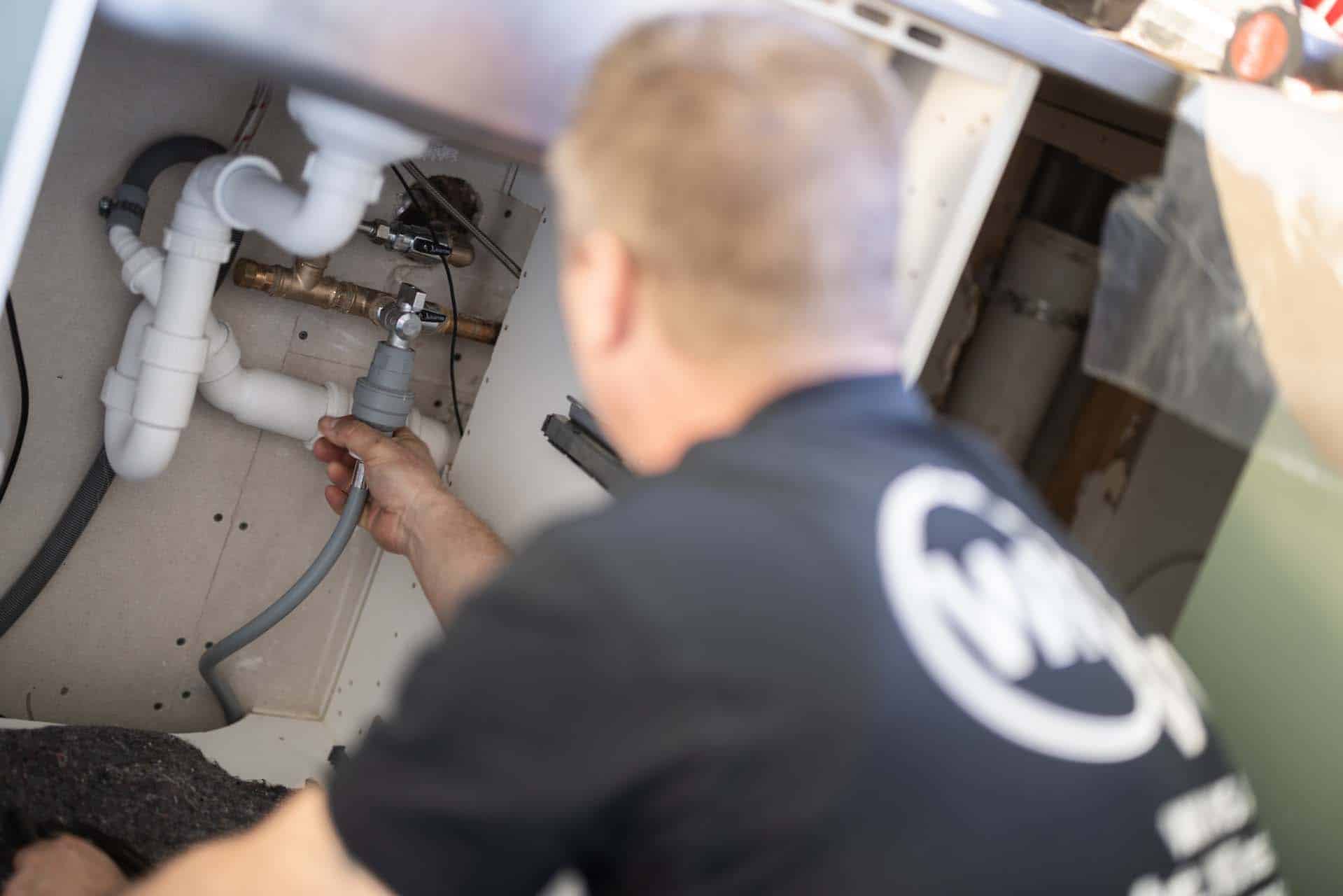 Håndværker fra WK VVS arbejder på rør under vask